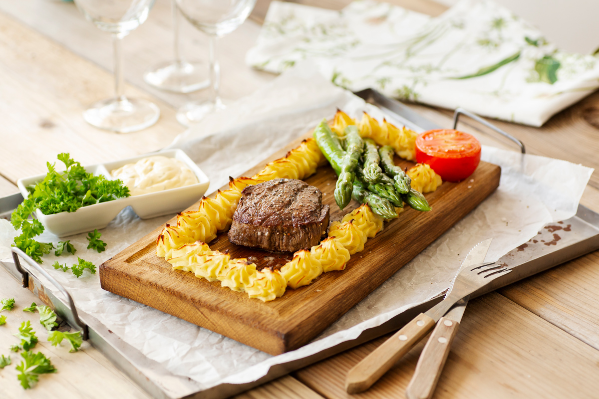 Elegant plankstek with beef tenderloin, duchess potatoes, asparagus and grilled tomato on a wooden board